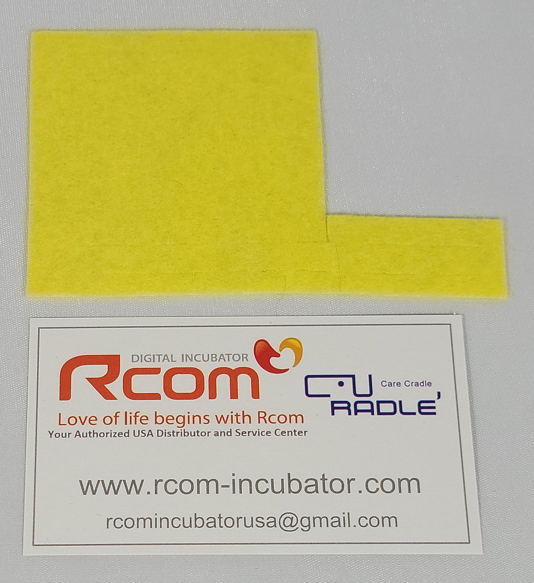 A yellow humidity pad alongside a business card with Rcom Incubator details.